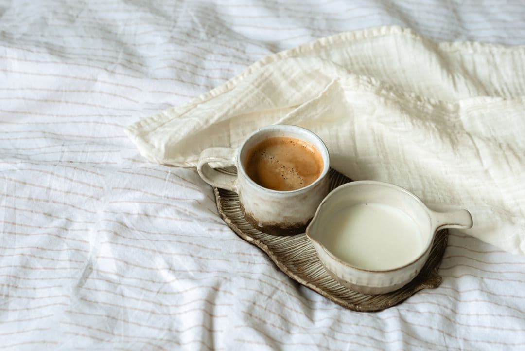 Café e leite em louça artesanal sobre lençol de linho.